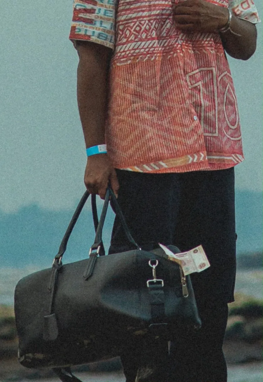Détail de la chemise Mokonzi Paradoxe portée, sac en cuir noir à la main, au bord du fleuve
